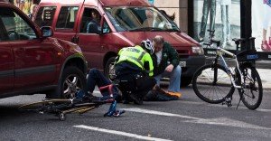 An EMT and another man assisting a biker in a crosswalk after a crash.