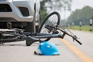 Close-up of a wrecked bike and helmet in front of a car on the street.