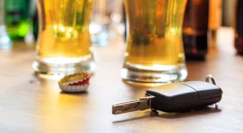 Car key on a wooden table, with glasses of beer and bottle caps in the background