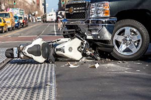 A white motorcycle crushed by a black truck on the street.