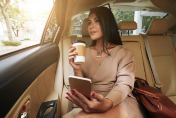 woman drinking coffee with phone in hand sitting in the back seat