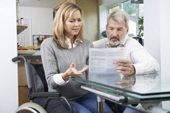 Woman In Wheelchair Reading Medical Bill With Husband