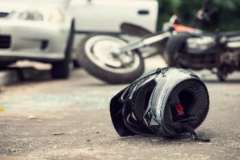 Close-up of a motorcycle helmet on the street with a wrecked car and motorcycle in the background